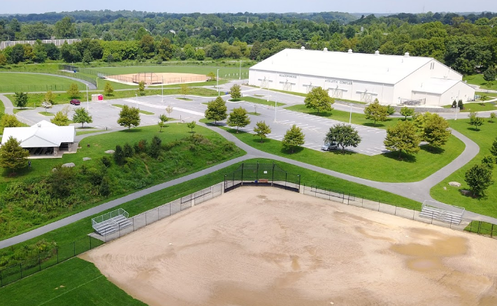 An aerial view of a baseball field in a park with a large white building in the background.