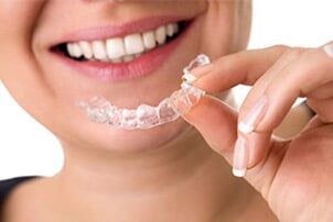 Smiling Female Holding Invisible Teeth Braces - general dentistry in Schererville, IN Smiling Female Holding Invisible Teeth Braces - general dentistry in Schererville, IN