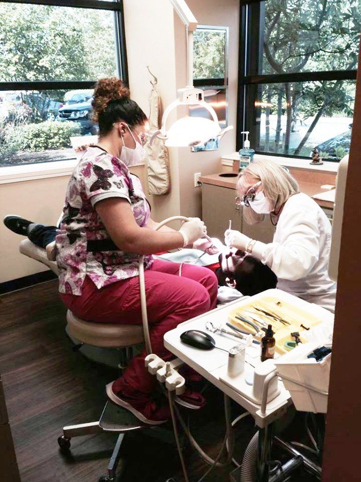 Dentist treating a patient in a bright clinic, with dental tools and a window view outside.