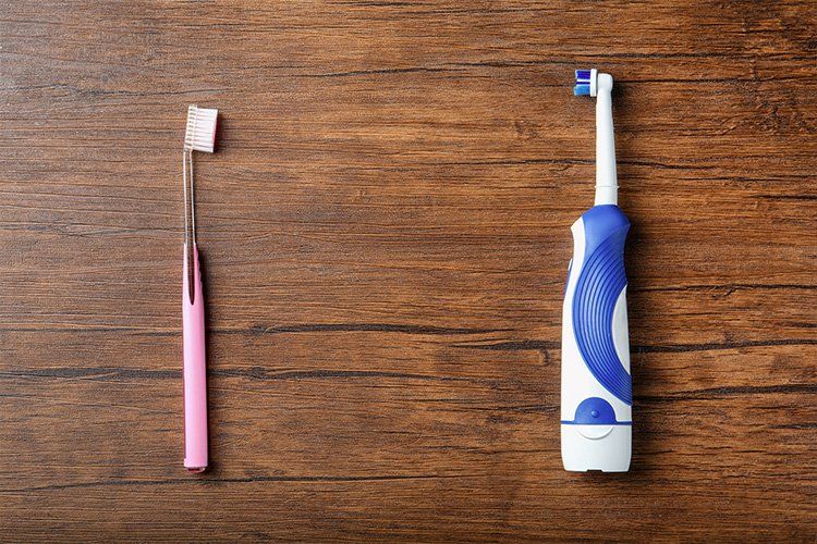 Pink manual toothbrush and blue electric toothbrush on a wooden surface