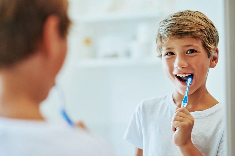 Child brushing teeth and smiling at a bathroom mirror with a blue toothbrush