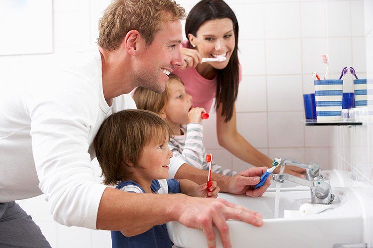 Family brushing teeth together at a bathroom sink with toothbrushes and toothpaste.
