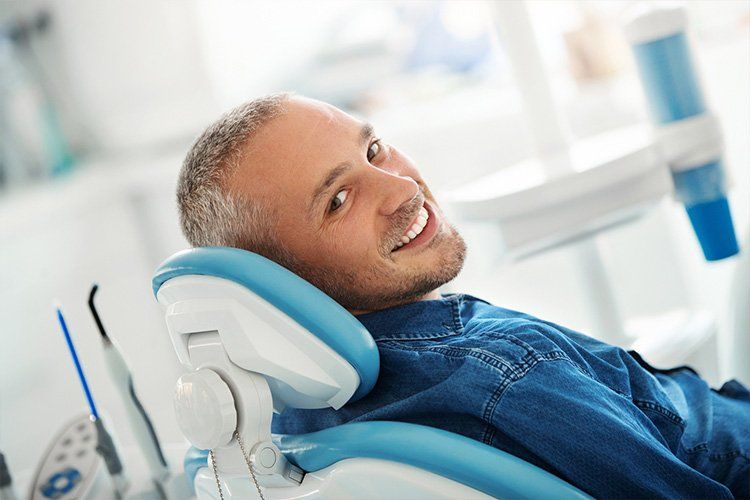 Man reclining in a blue dental chair, smiling in a bright dentist office