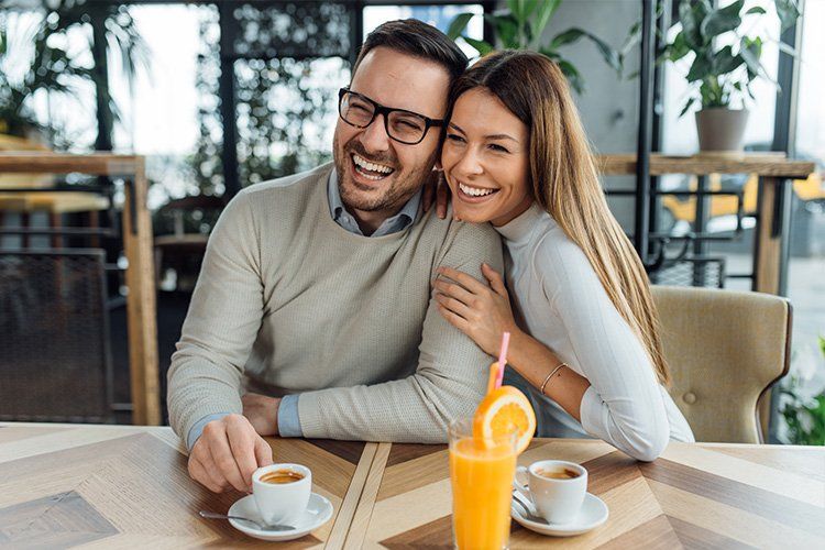 Smiling couple seated at a café table with coffee and orange juice