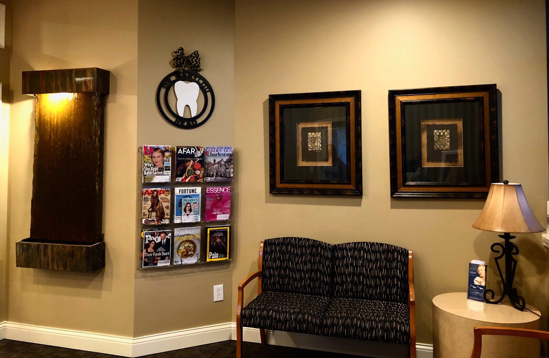 Clinic waiting room with wall art, brochures, a bench, and a lit table lamp.
