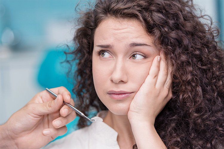 Dentist holding a dental pick near a worried patient with a hand on her cheek