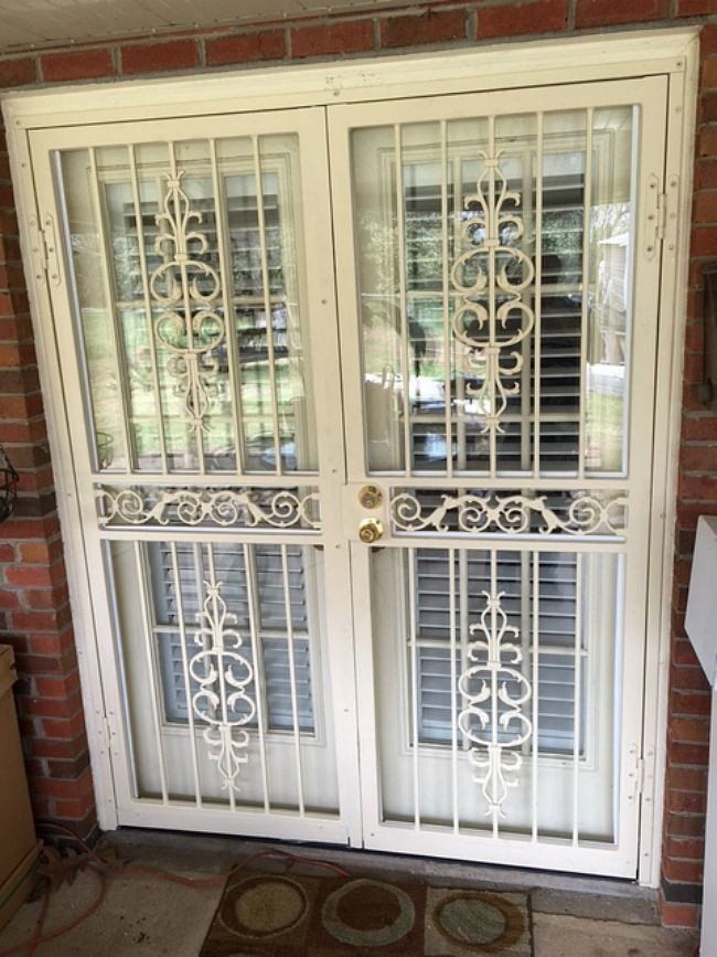 a white door with a wrought iron gate is sitting on a brick wall .