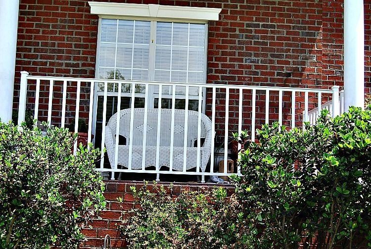a white wicker couch is sitting on a porch of a brick house .