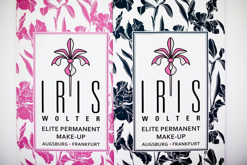 Zwei Logos von IRIS WOLTER Elite Permanent Make-up, eines in Rosa und eines in Schwarz, auf floralem Hintergrund