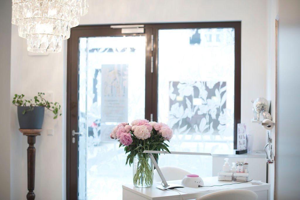 Heller Eingang mit Glastür, weißem Tisch und rosa Blumen in einer Vase in der Nähe des Fensters.