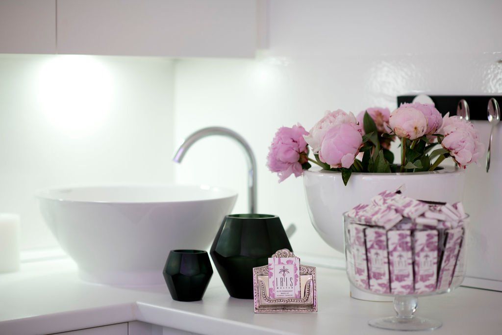 Weißes Waschbecken und Blumen auf einer sauberen Arbeitsplatte mit rosa Dekoration und schwarzen Kerzenhaltern.