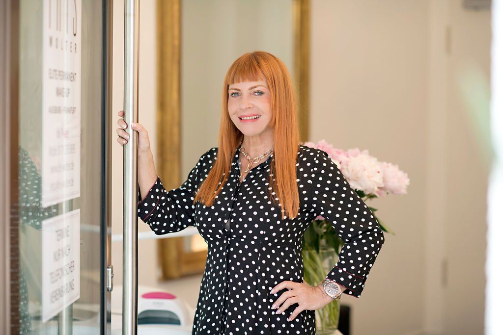 Iris Wolter in einem schwarzen Kleid mit weißen Punkten steht an einer Tür in einem hellen Flur.