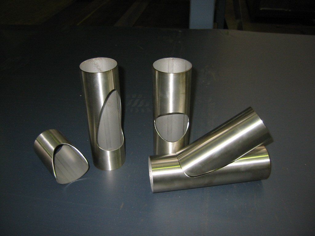 Several shiny, cut metal tubes arranged on a dark surface. They are various lengths, some with angled cuts.