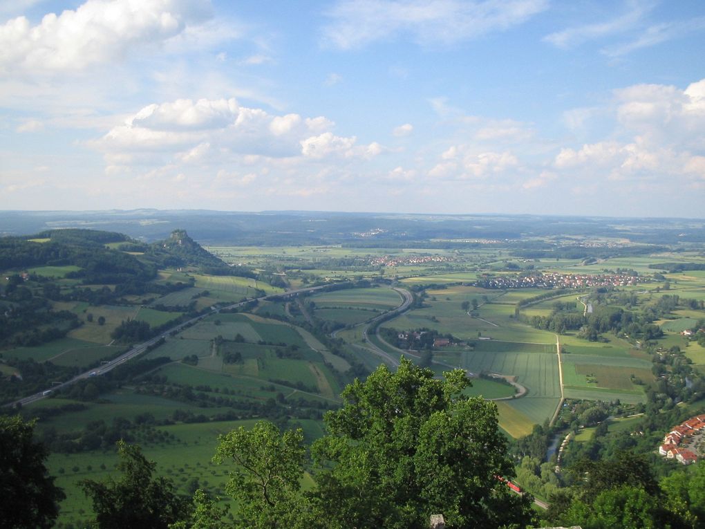 Malerische Aussicht auf ein Tal mit grünen Hügeln, einer Autobahn und einer Stadt unter einem bewölkten blauen Himmel.