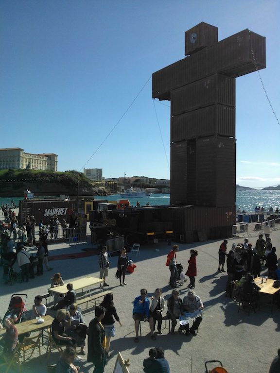 Ein aus Containern gebauter Mann am Hafen in Marseille, viele Menschen rundherum.
