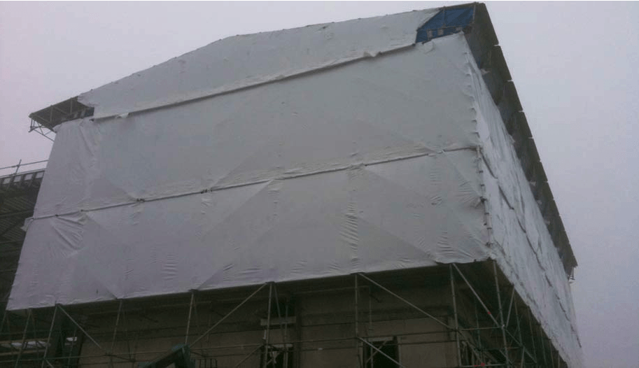 Een groot gebouw is bedekt met steigers en een wit zeil.