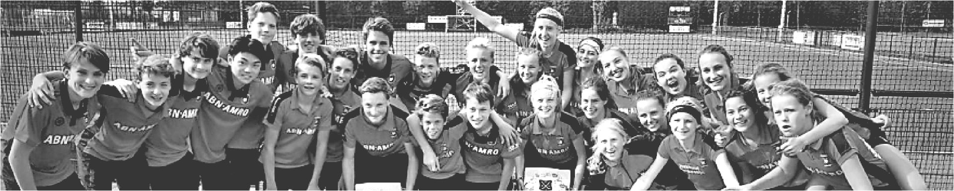 Een groep mensen poseert samen in de buitenlucht; sommigen lachen, anderen omhelzen elkaar.