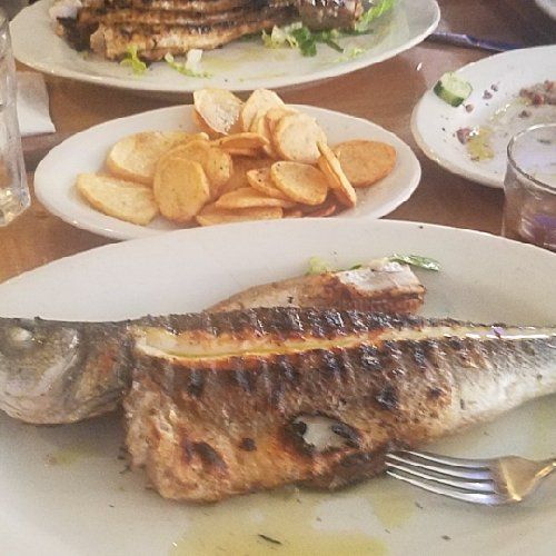 A plate of fish with a fork on a table with other plates of food