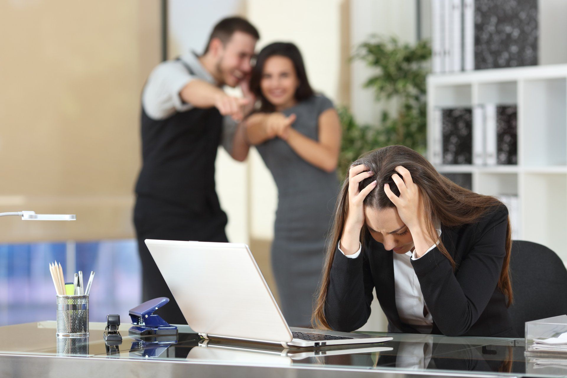 Pestgedrag op het werk? Maak gebruik van een MfN-registermediator Twee zakenlieden pesten een trieste collega die zit op haar werkplek op kantoor