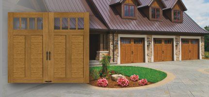 Wooden garage doors with glass panes, a house with a brown roof, and a green lawn.