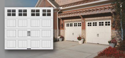 White garage doors with windows in a brick home. Two sets of doors with a decorative pergola.
