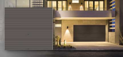 Modern house exterior with a closed gray garage door and a lit driveway at night.