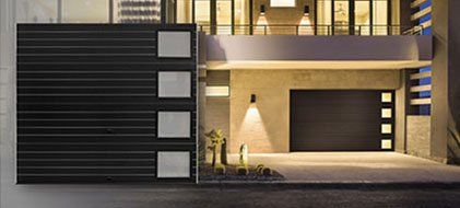 Modern home exterior with illuminated garage doors and front gate.
