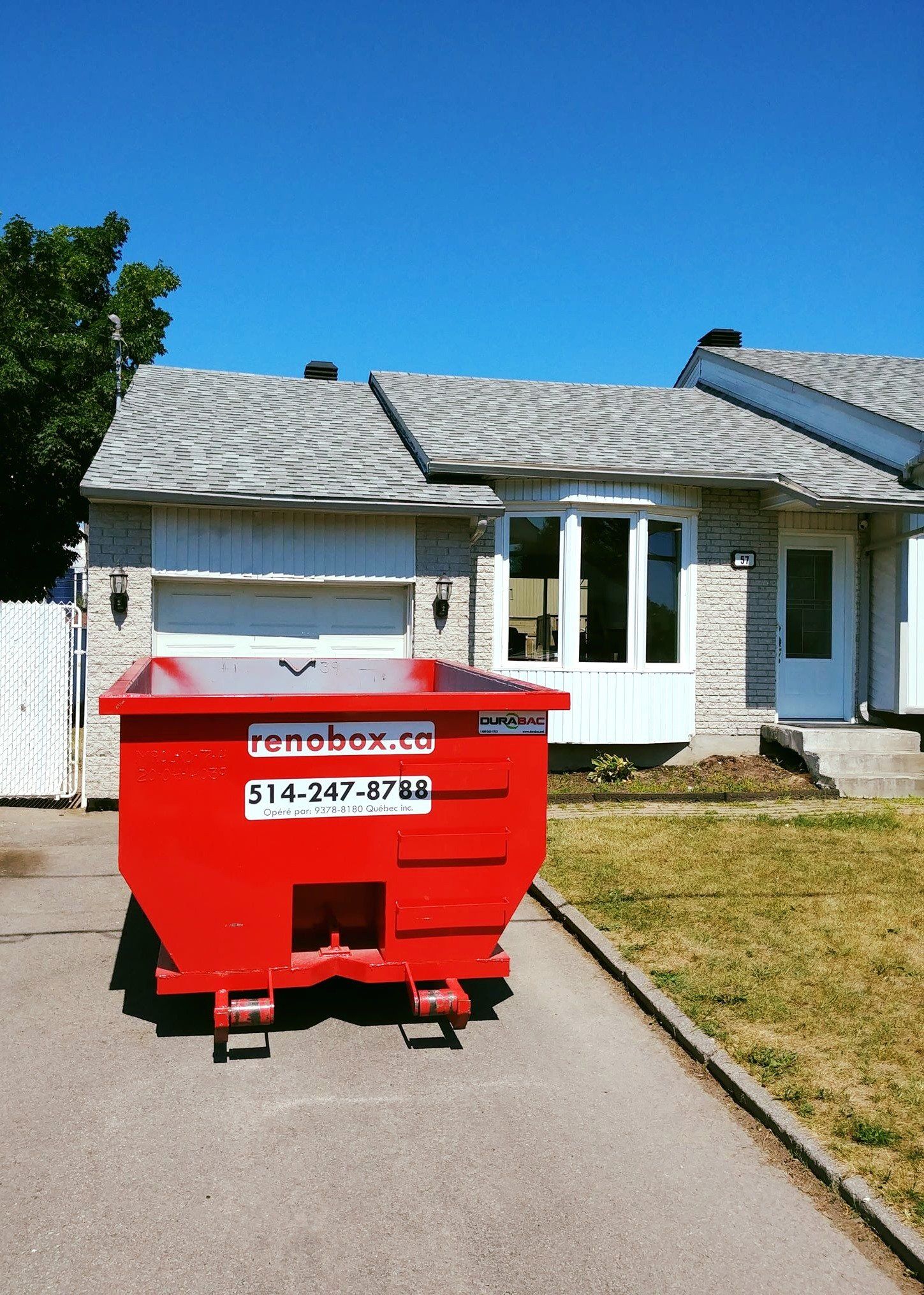 Une benne à ordures rouge devant une maison par une journée ensoleillée.