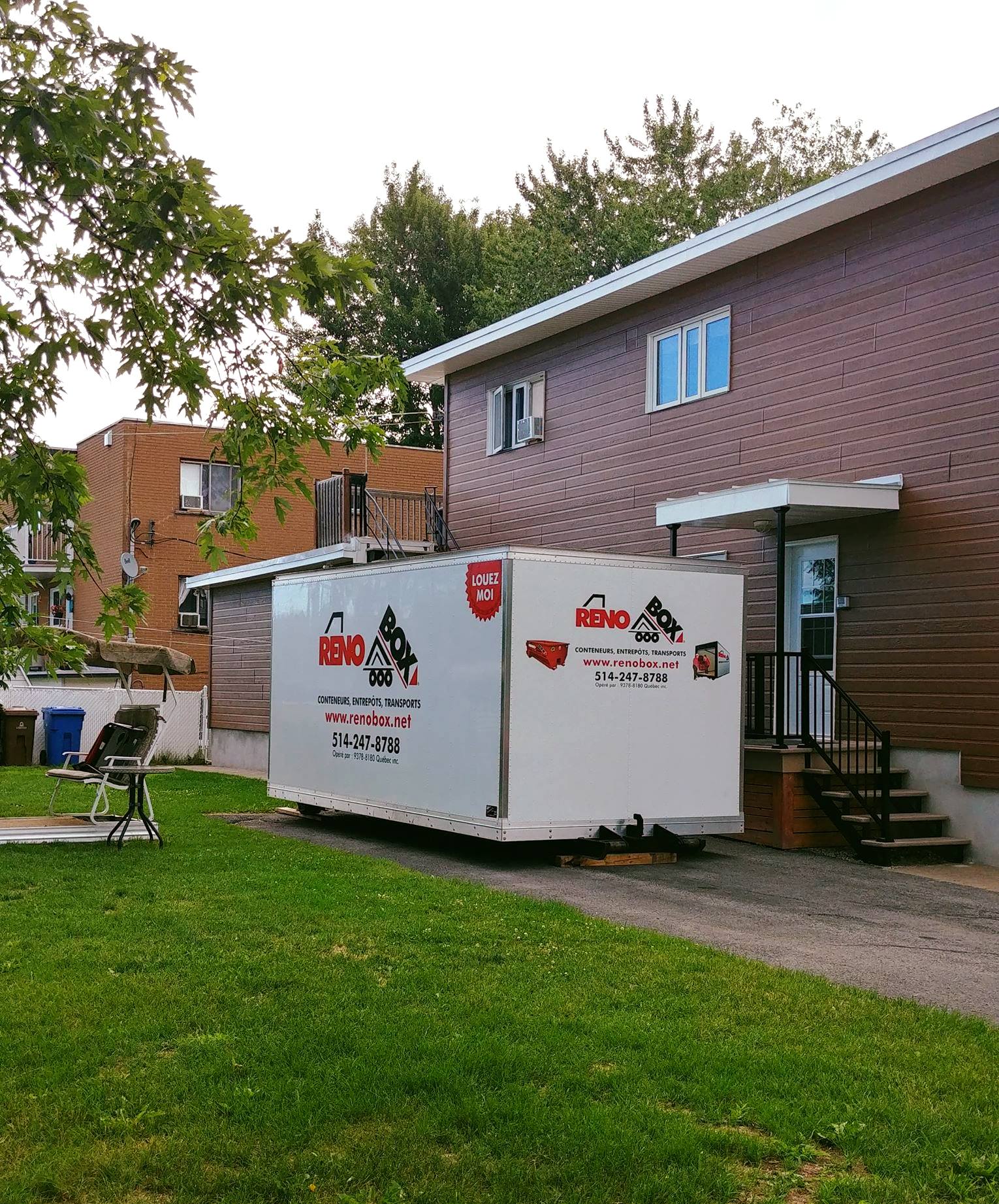 Un conteneur de stockage blanc est stationné à côté d'un bâtiment en briques et d'une pelouse.
