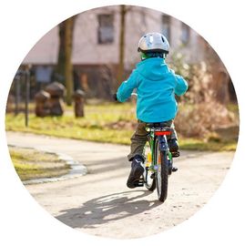 Child wearing a turquoise jacket riding a bike