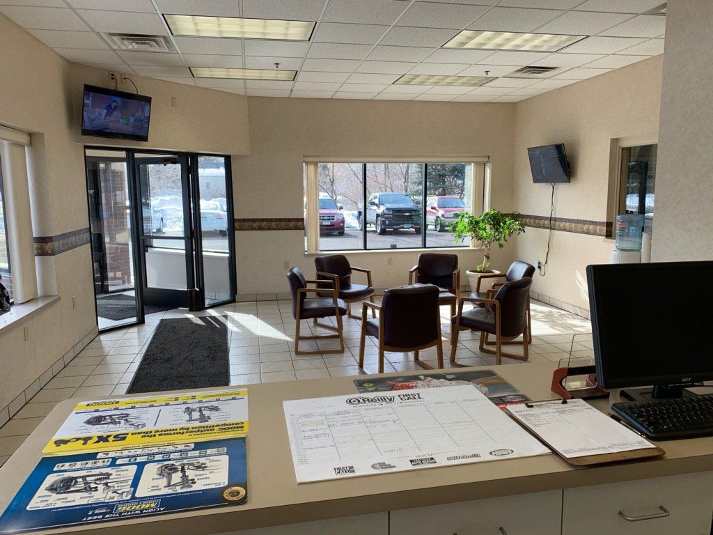 Waiting area in an auto shop: chairs arranged around a table, window overlooking cars, TV on the wall.