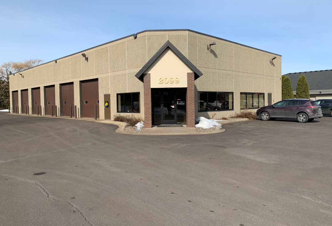 Tan commercial building with brown garage doors and a glass entryway. A car is parked out front.