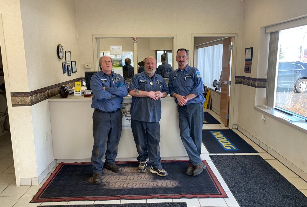 Three men in blue uniforms stand inside a business, posing near a counter.