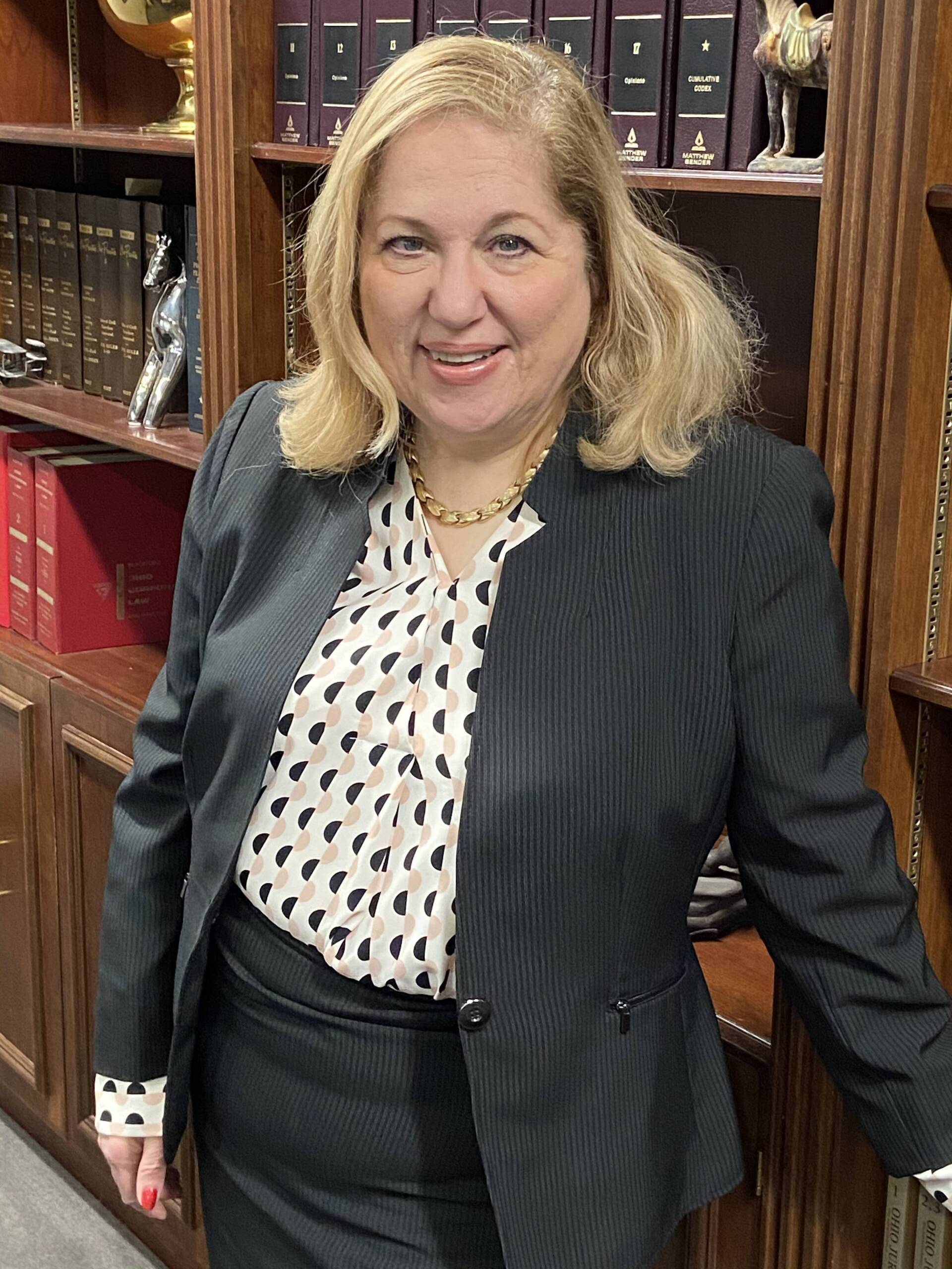 Woman in a black suit standing in front of bookshelves, smiling at the camera.