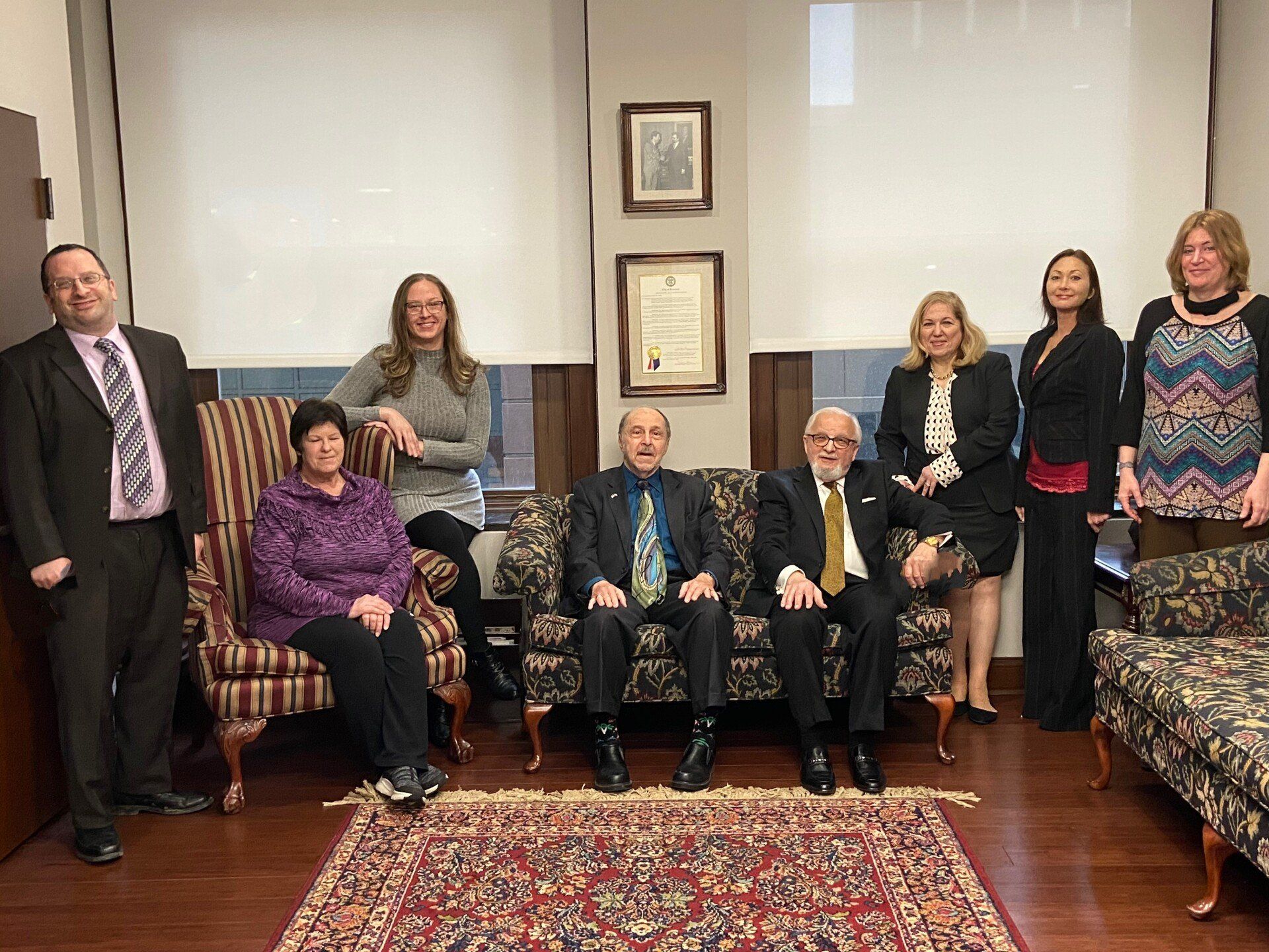 Group seated and standing in a formal room with framed art and patterned chairs