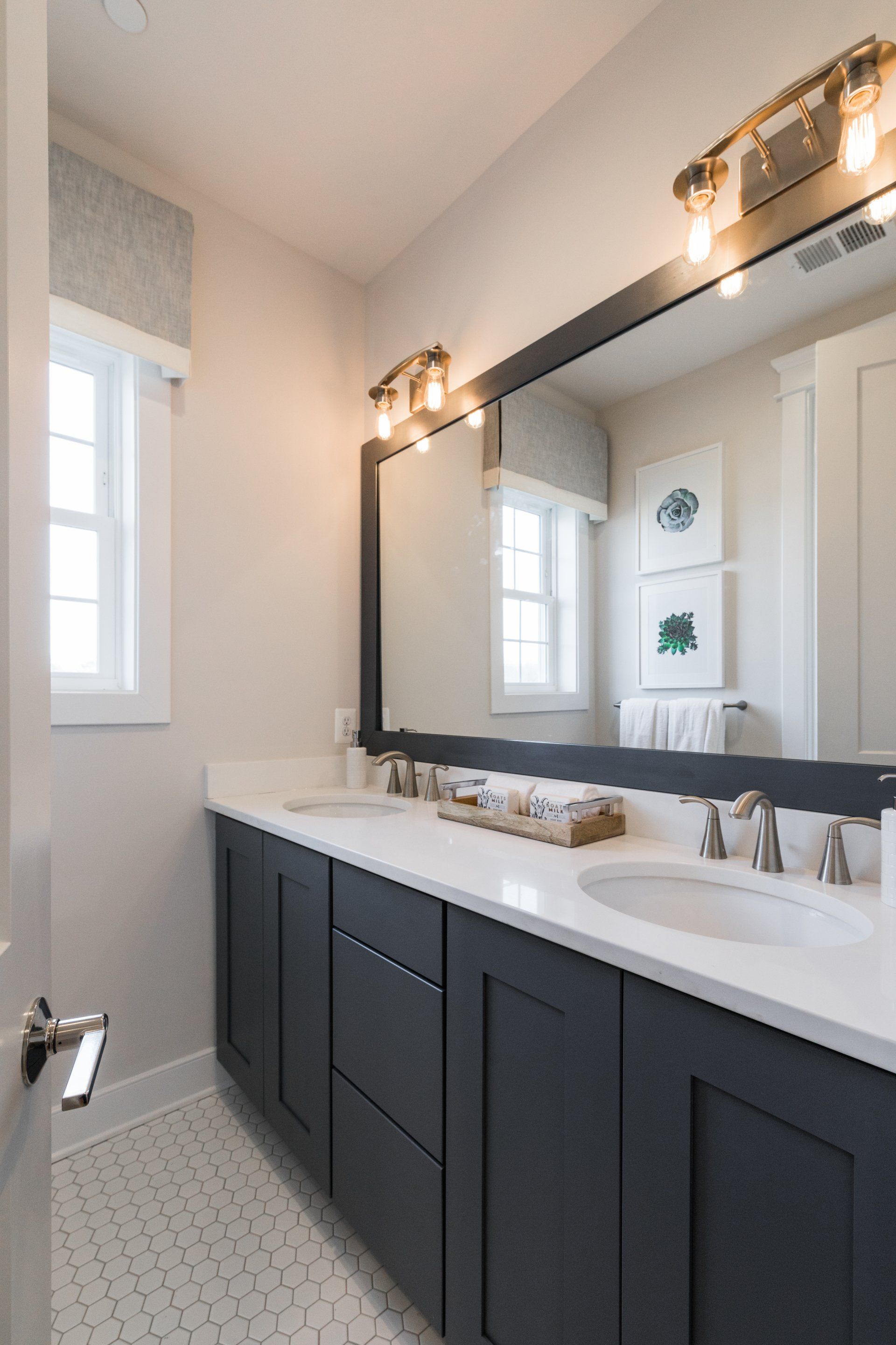 Bathroom with dark blue cabinets, white countertop, large mirror, and hexagonal tile floor.