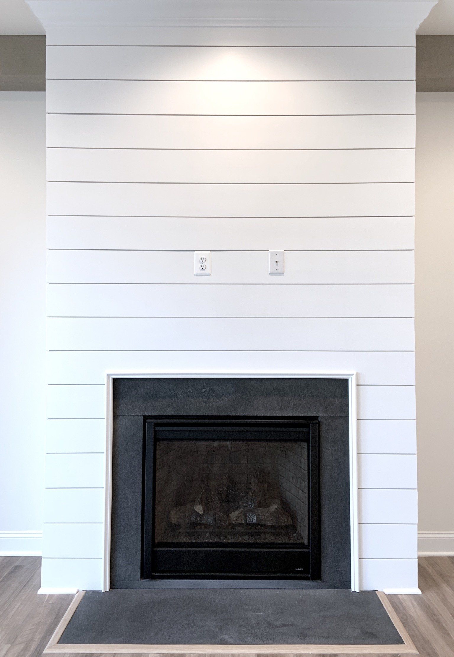 White fireplace with shiplap accent wall, dark gray hearth, and a black fireplace insert.