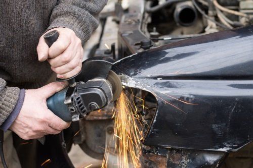 due mani con un flessibile al lavoro sulla carrozzeria di un'auto