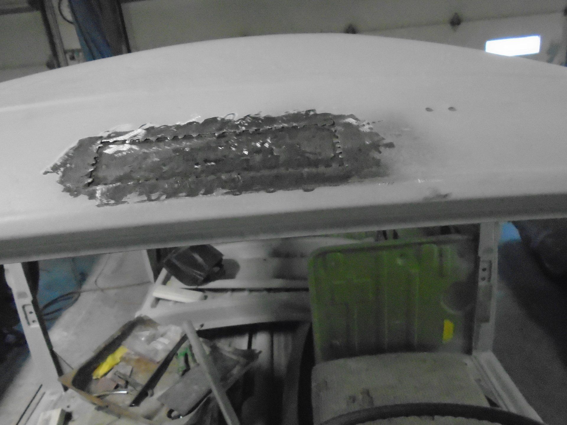 A car roof with a rectangular metal patch. The car is gray, in a workshop setting.