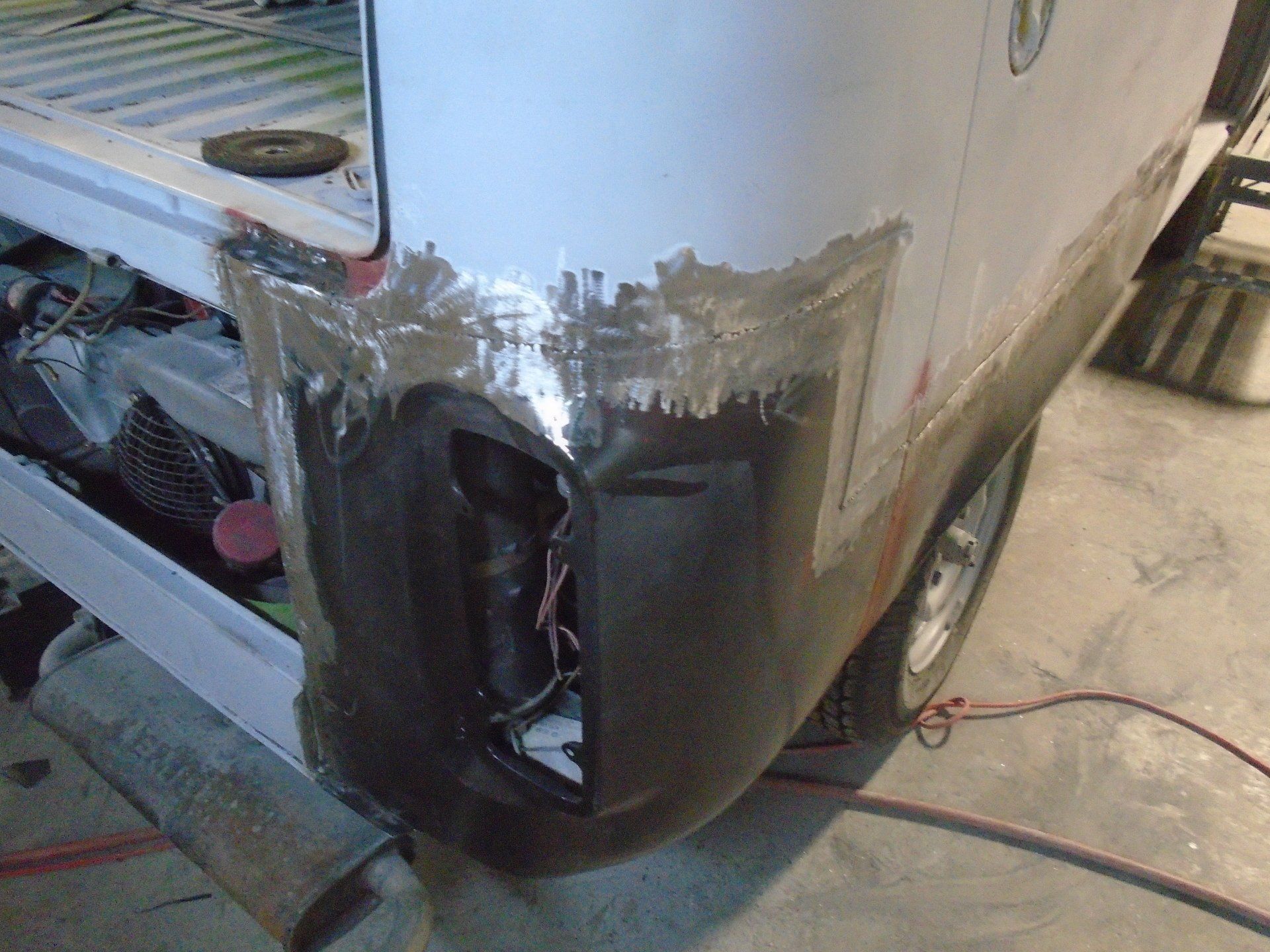 Damaged white vehicle body panel, exposing a tail light and repair work in progress.