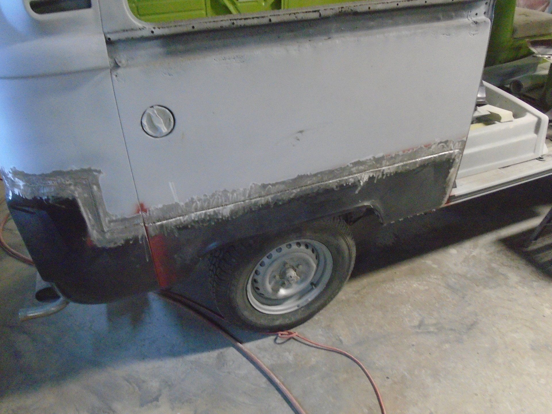 Partially-restored vehicle body with grey, black, and white paint; a wheel and gas cap are visible.