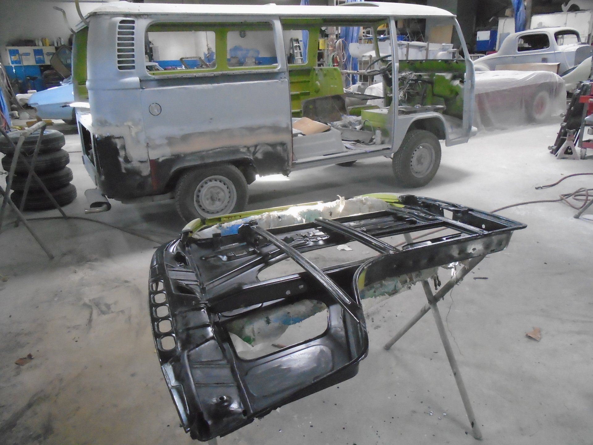 VW van undergoing restoration in a garage; body partially disassembled with painted floor pan in foreground.