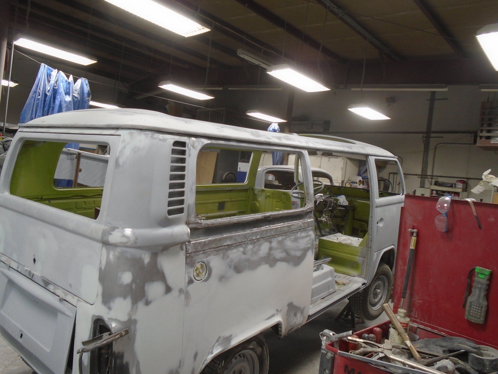 A gray and green Volkswagen bus in a repair shop. The body is partially disassembled.