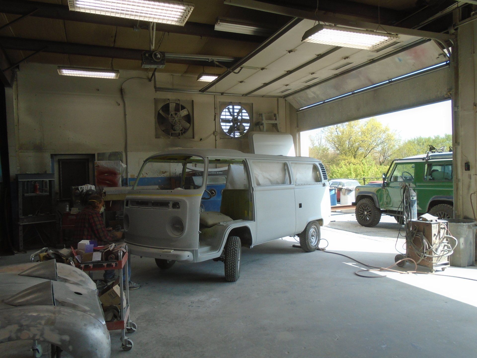 A partially restored white Volkswagen van inside a garage, with a green SUV visible behind it.