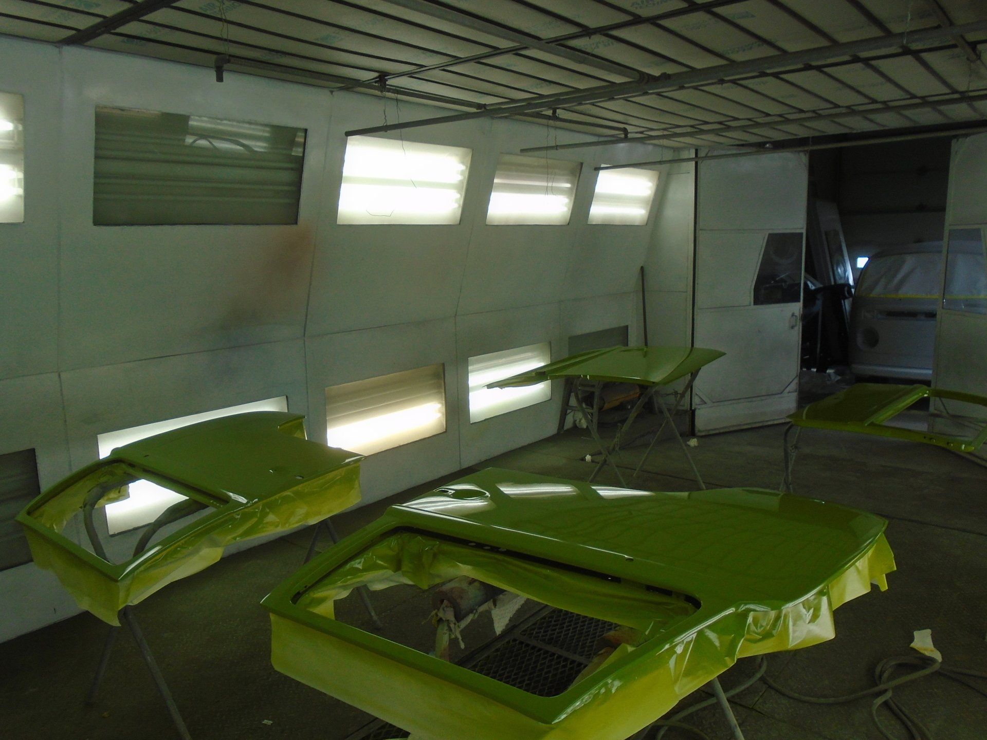 Lime green car parts in a spray paint booth, illuminated by overhead lights.