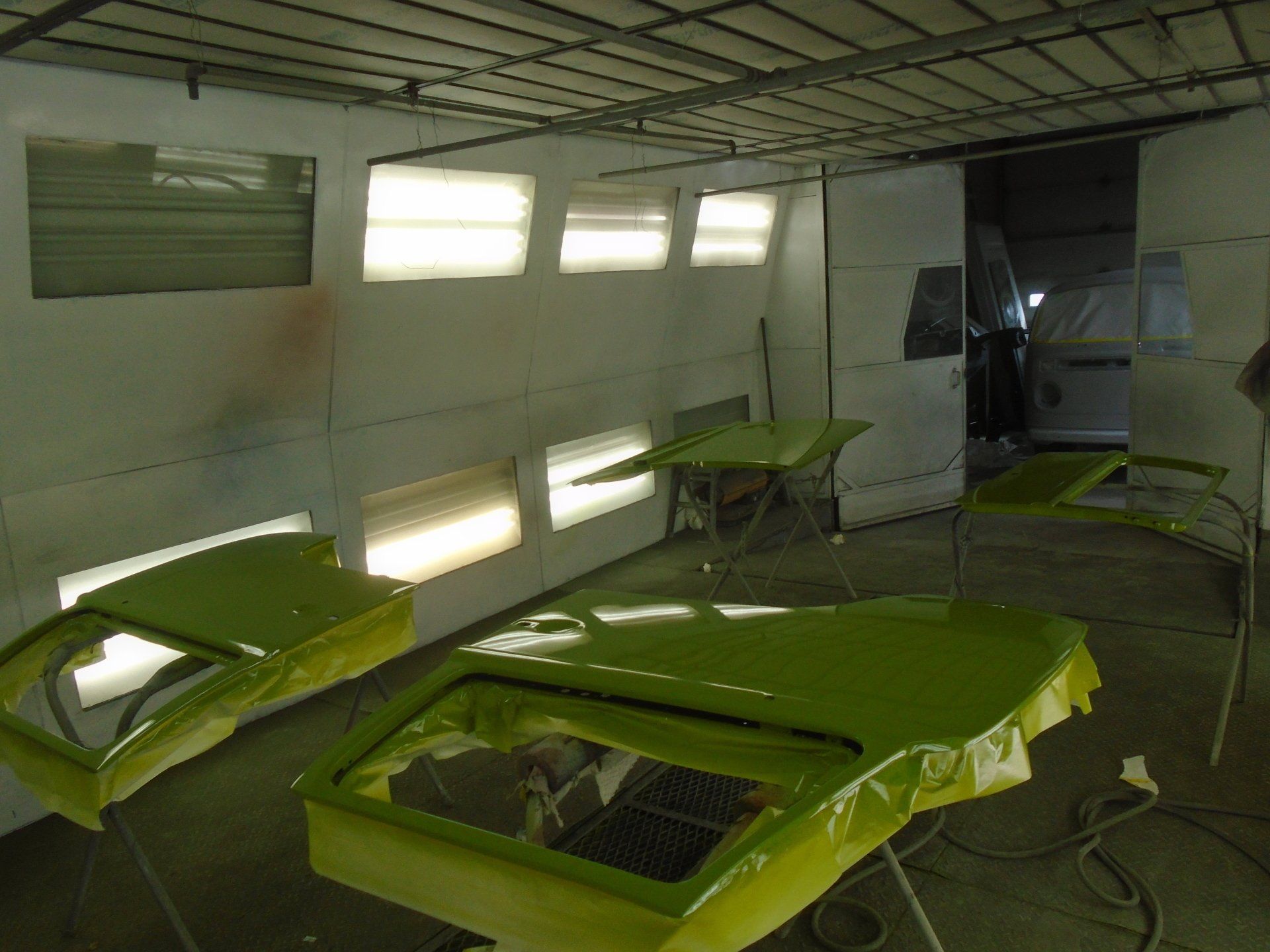 Car paint booth: green painted car doors and parts. Interior with bright overhead lights.