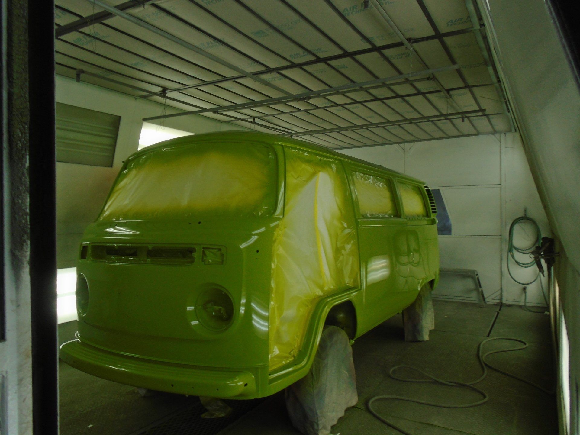 Green VW bus in a spray booth, partially masked for painting.