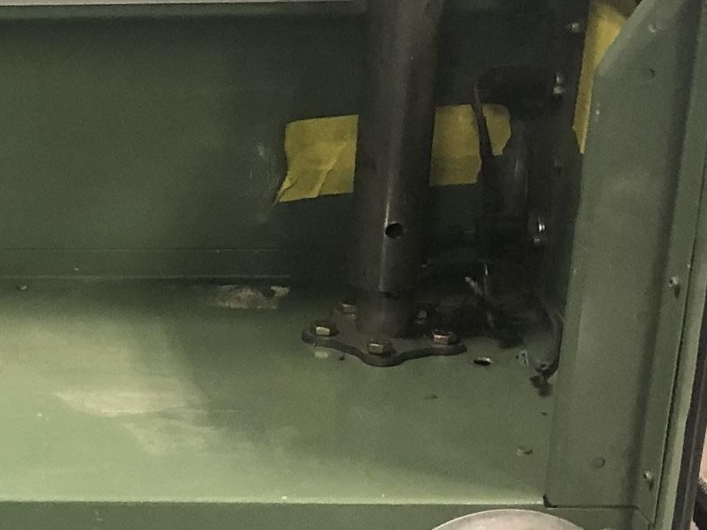 Dark metal structure mounted on a green metal surface, with visible screws and wiring. Yellow tape is also visible.