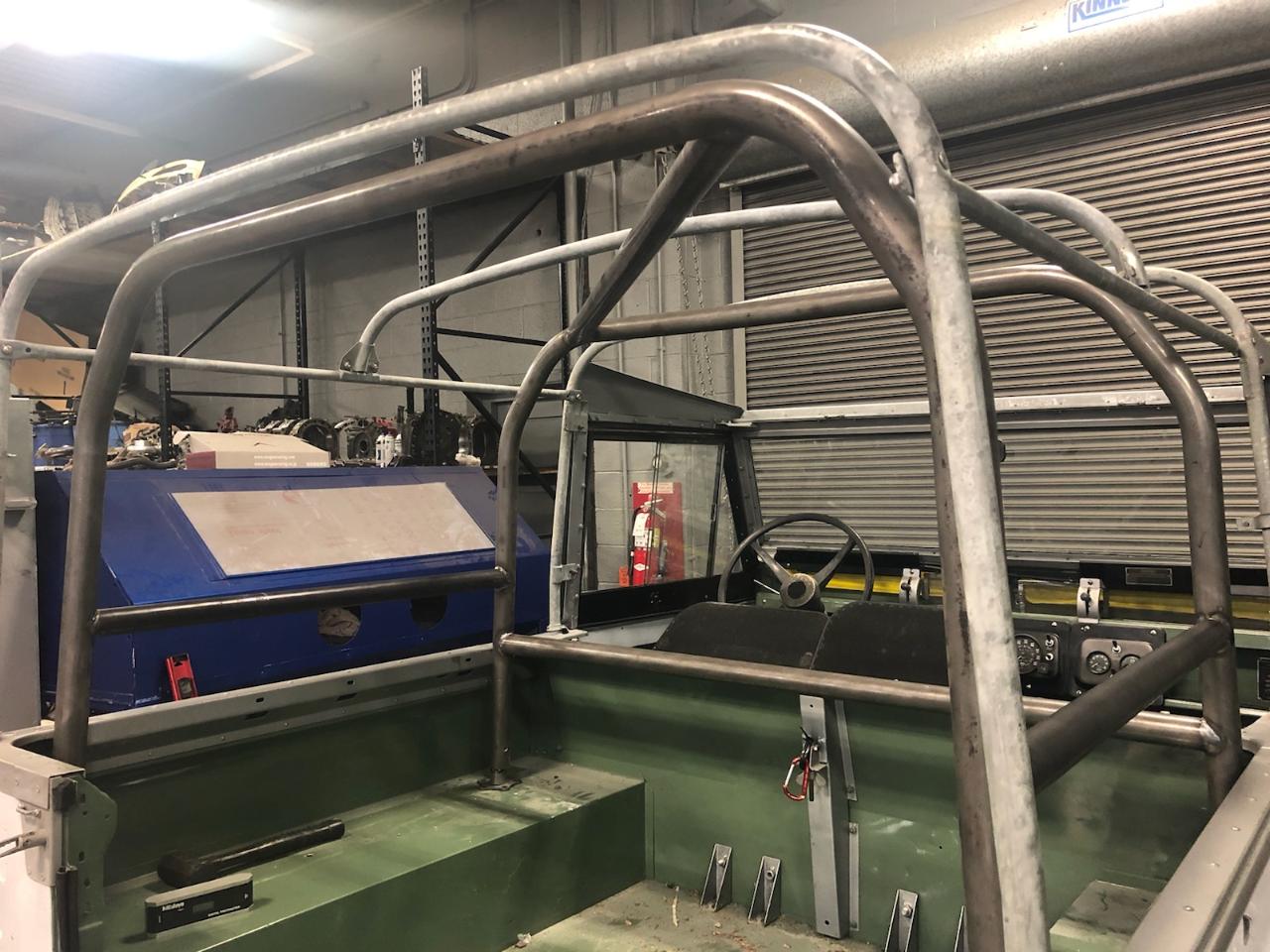 Metal roll cage frame installed in a green vehicle interior. Shop setting, partially completed.