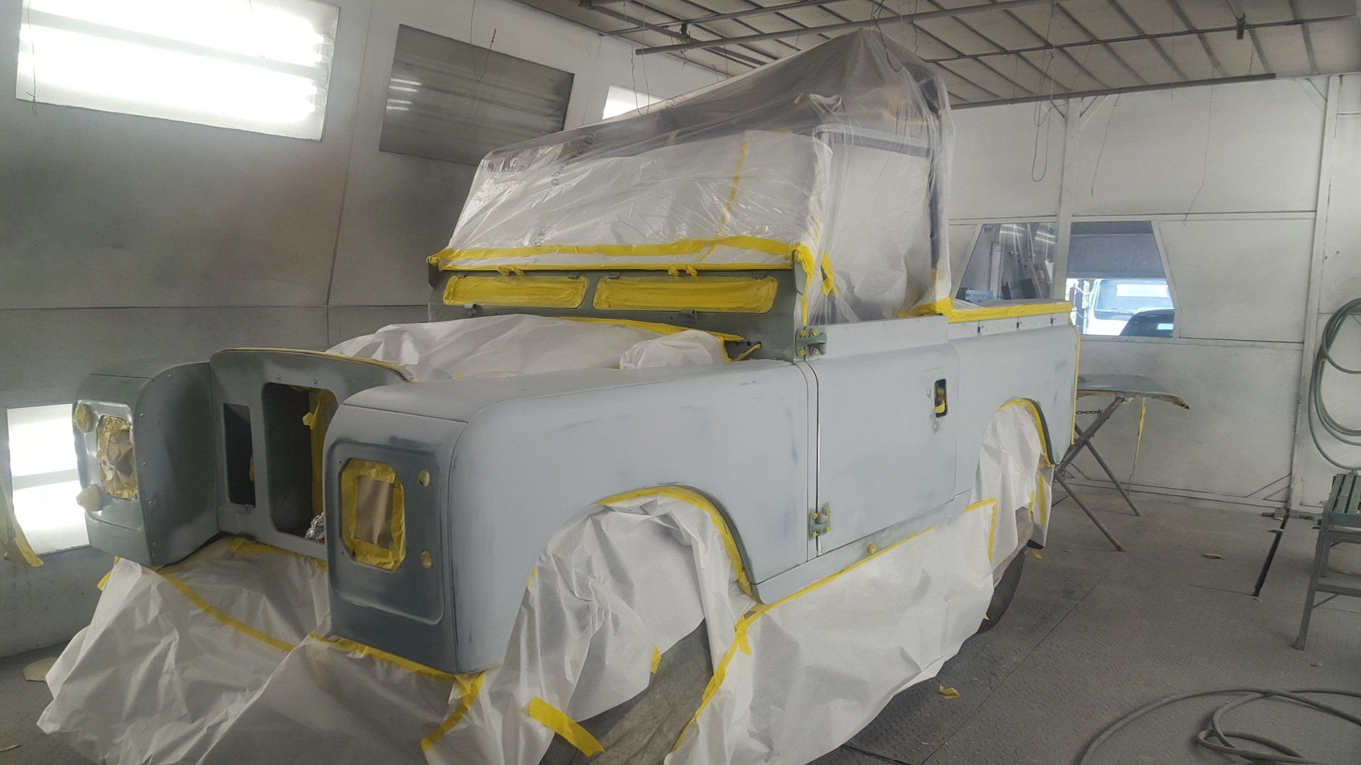 Land Rover in a paint booth, covered in plastic and tape, ready for paint.